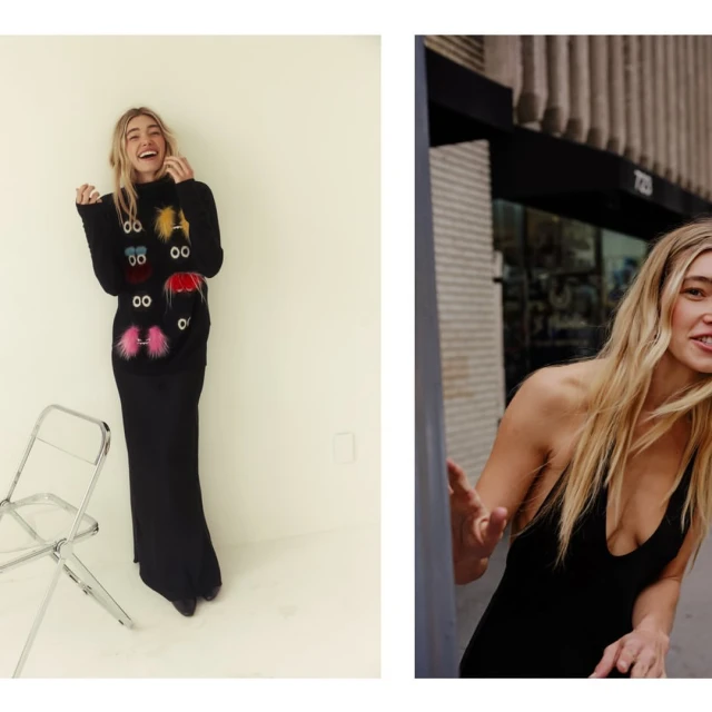 Smiling blond woman in black dress and patterned sweater poses in a brightly lit room, with another woman outside a building.
