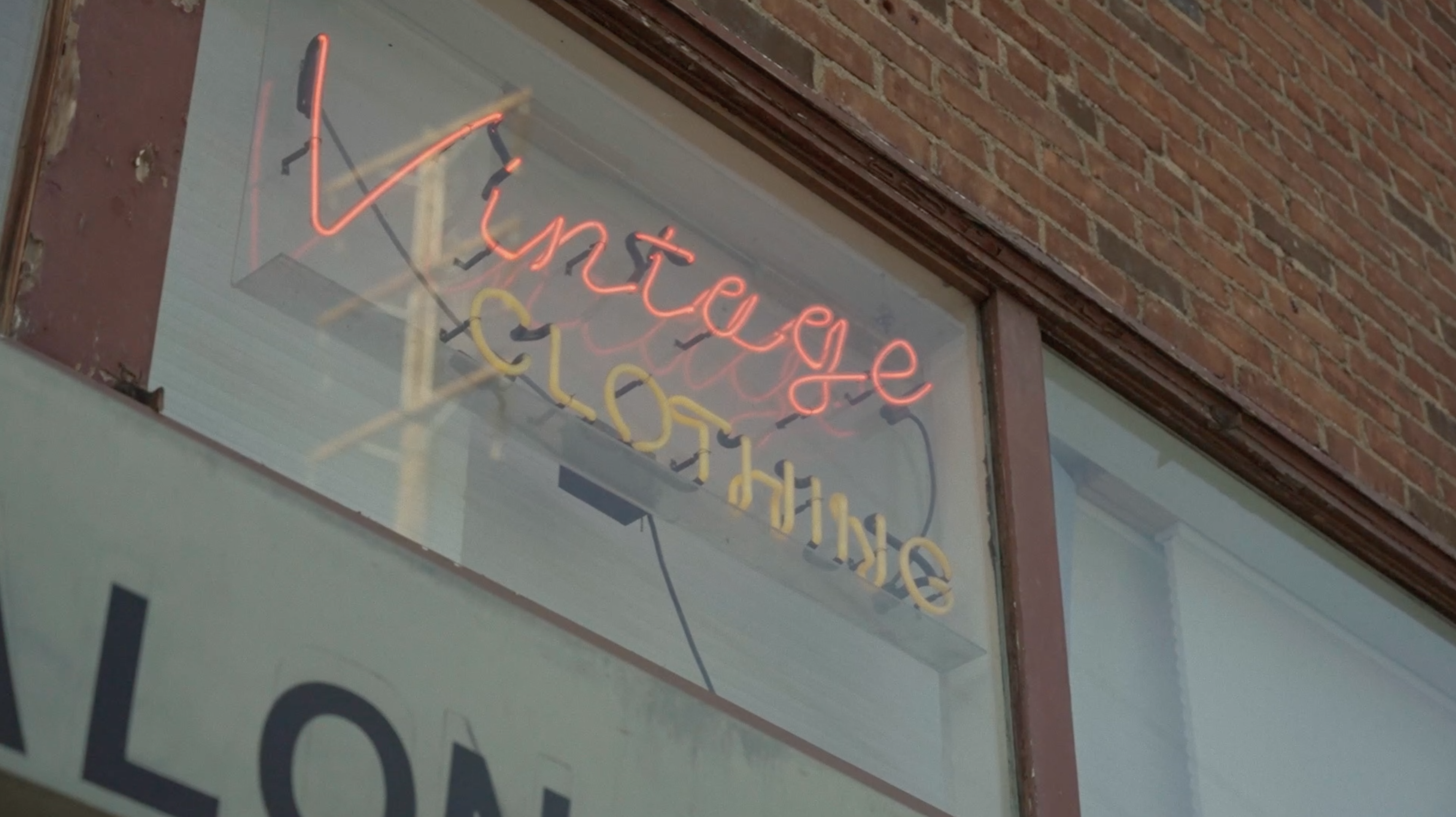 Vintage clothing store neon sign in window with brick wall. Advertising with bright and colorful vintage clothing sales.