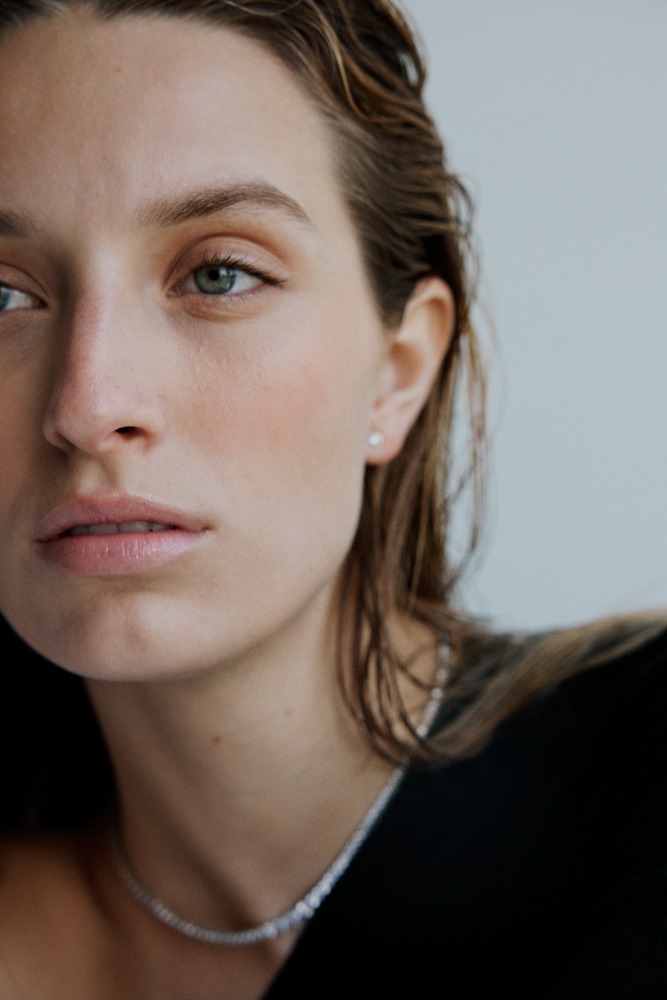 Close-up portrait of a woman with wet hair, wearing a black top and jewelry against a neutral background, focusing on beauty and fashion.