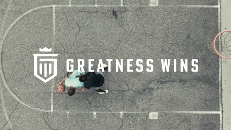Aerial view of two basketball players on an outdoor asphalt court with white painted lines and a basketball hoop.