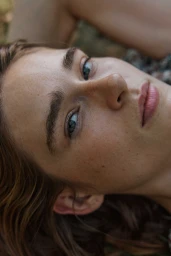 Close-up portrait of a young woman with natural makeup, light freckles, and dark brown hair photographed from above by Kate Moore.