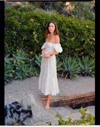 Woman in white off-the-shoulder midi dress standing outdoors with a fluffy dog in the foreground by photographer Kate Moore