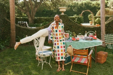Two women smiling at an outdoor garden party with a picnic table set with food and green check tablecloth.