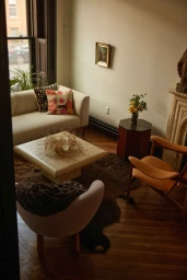 Cozy living room interior featuring a light beige sofa, coffee table, armchairs, and a small fireplace mantle photographed by Kate Moore