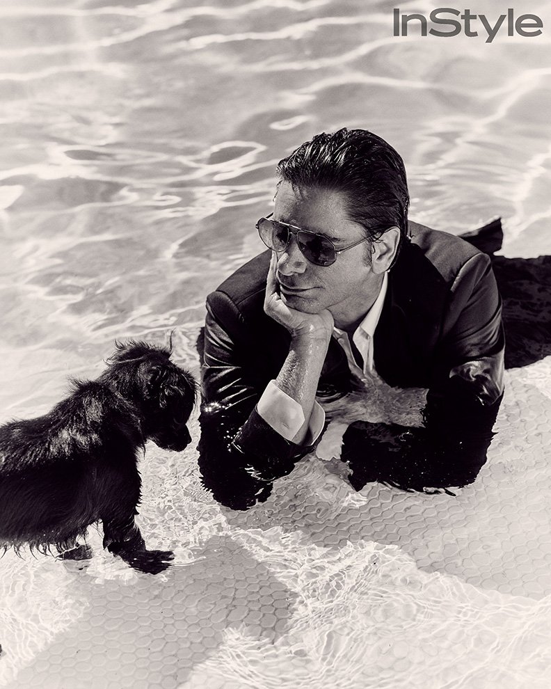 Black and white portrait of a man in a suit and sunglasses reclining in a pool next to a small dog, for InStyle magazine.