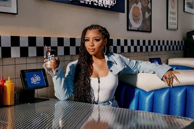 A young woman in a diner booth holds a Pepsi can, with a checkerboard wall and soda-shop details creating a vintage atmosphere.