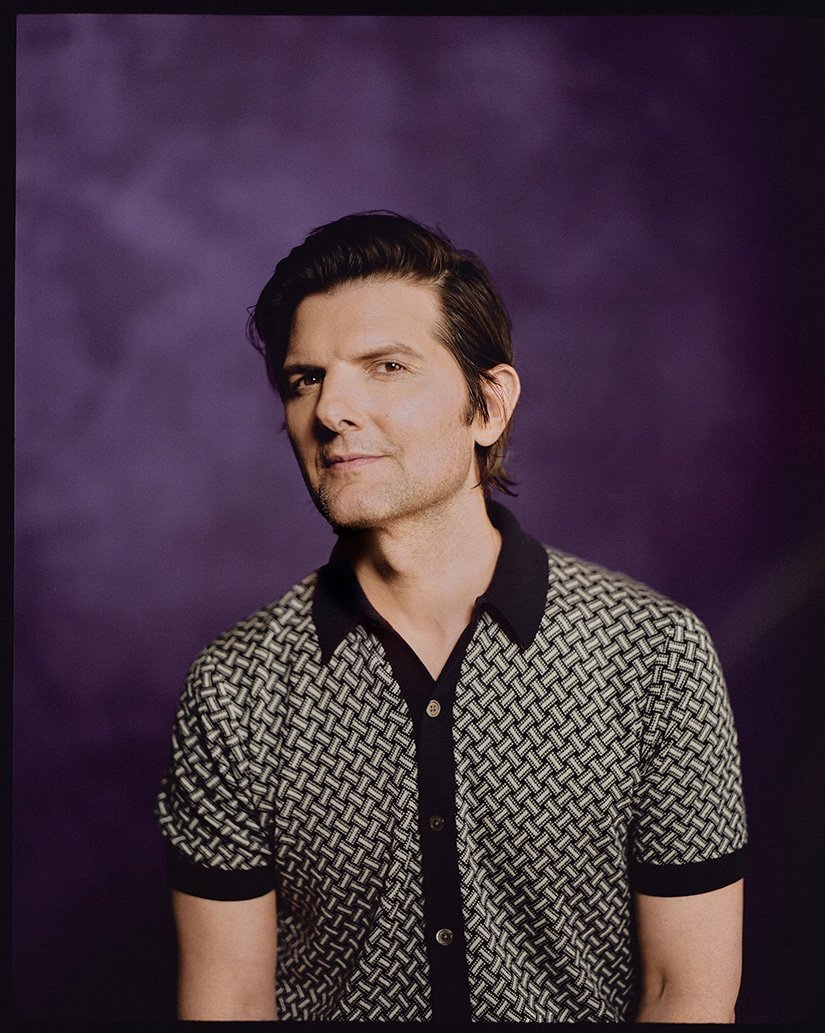 Portrait of Adam Scott in a patterned shirt against a purple backdrop, capturing his engaging gaze and confident demeanor in a studio setting.