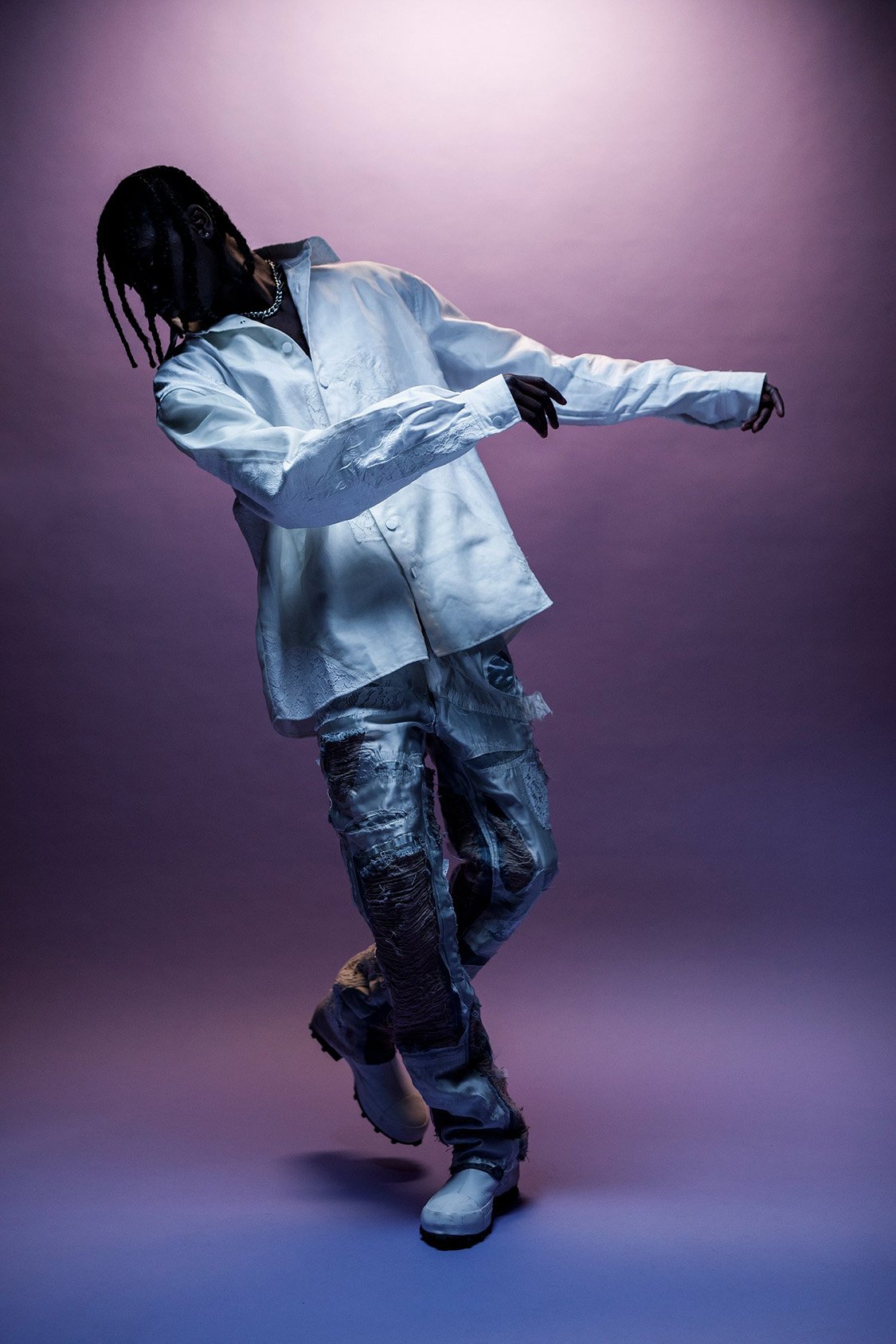 Man poses in white button-down shirt and printed pants against a gradient purple backdrop in a studio setting.