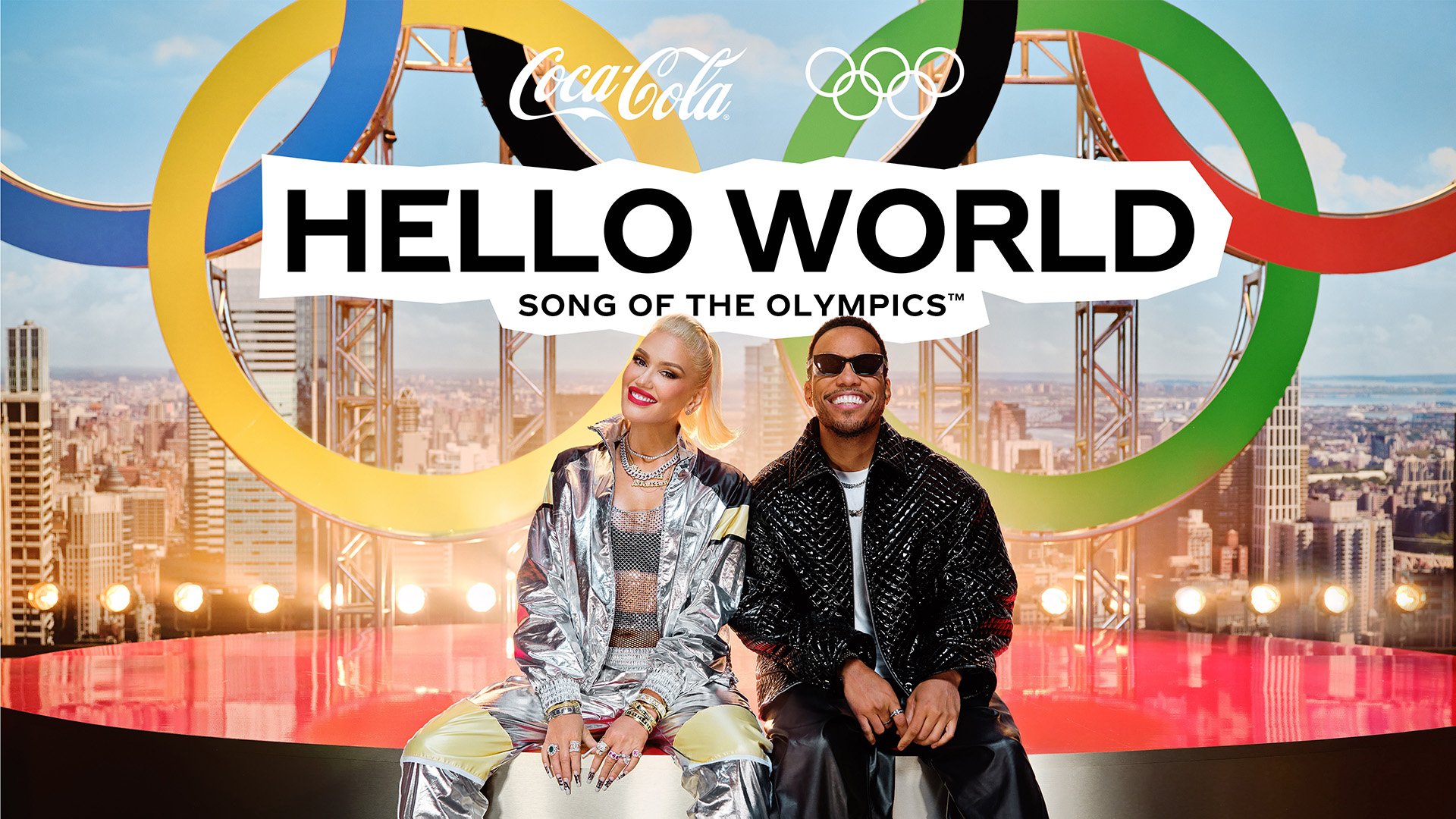 Coca-Cola Olympic promotional image of Gwen Stefani and Taio Cruz sitting in front of a backdrop of a city skyline and Olympic rings.