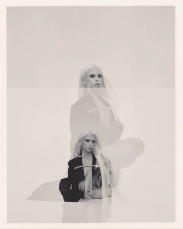 Monochrome multiple exposure portrait of a blonde woman wearing a dark blazer and hoop earrings against a light background.