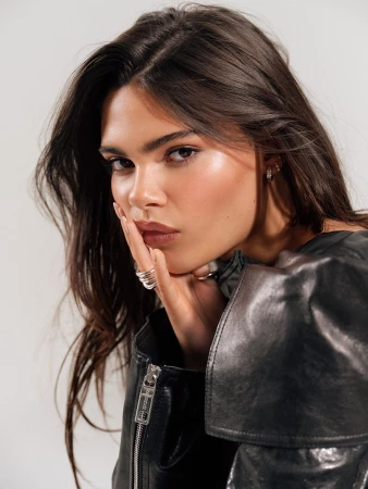 Close-up portrait of a woman with dark hair wearing a black leather jacket with her hand near her face by Alex G. Harper.
