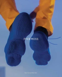 Close-up low-angle shot of blue sneakers with textured rubber soles and bright yellow trousers against a blue gradient backdrop.