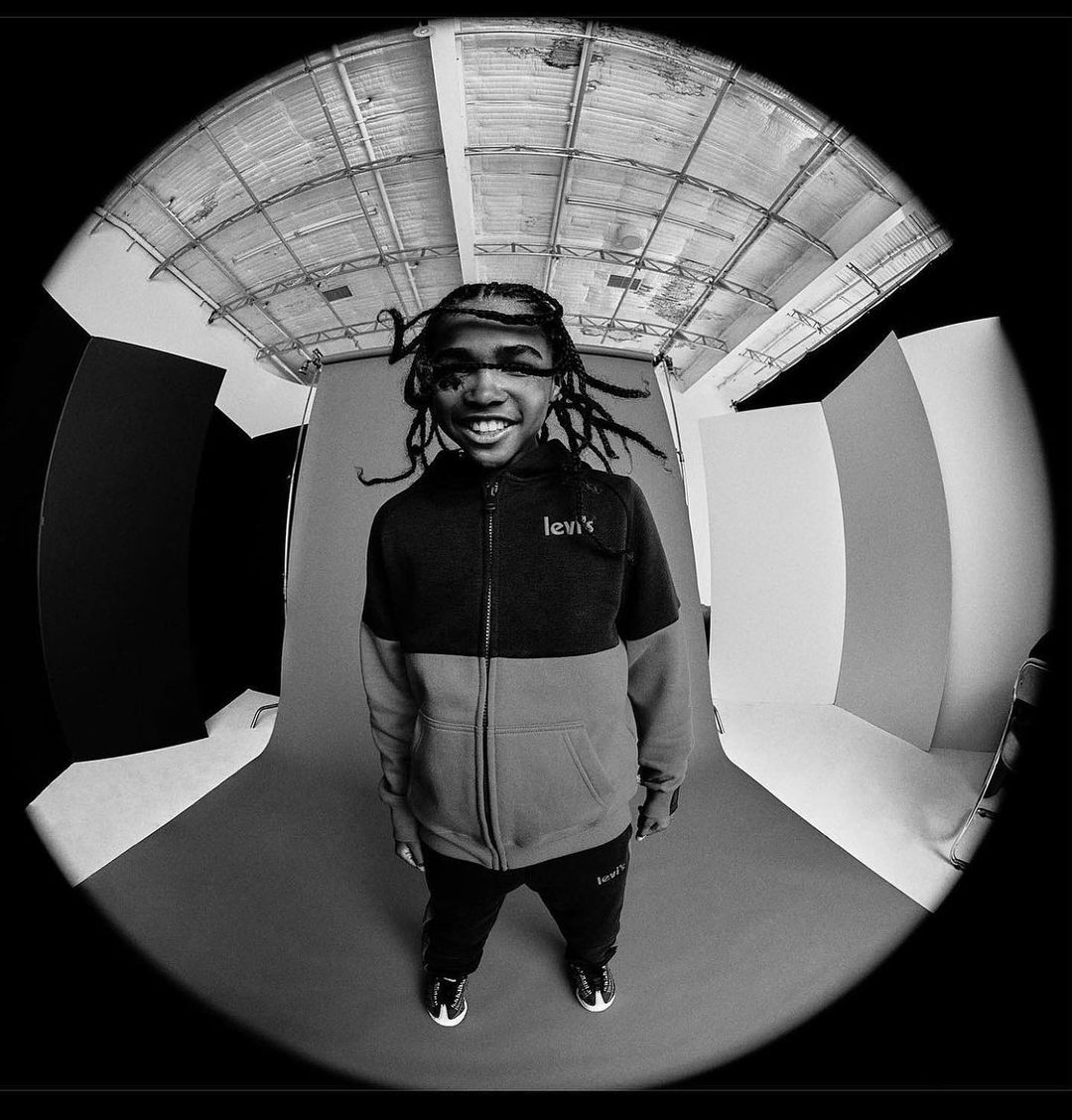 Youthful individual in a color-blocked Levi's tracksuit, captured with a fisheye lens in a photo studio setting. Black-and-white image.
