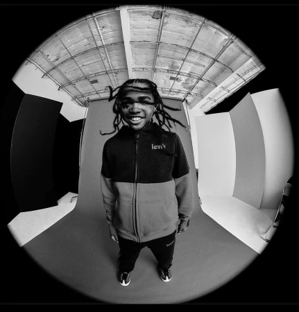 Youthful individual in a color-blocked Levi's tracksuit, captured with a fisheye lens in a photo studio setting. Black-and-white image.