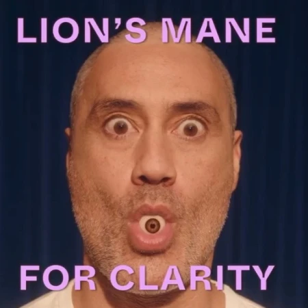 Close-up of a bald adult male with an eye in his mouth, set against a dark blue curtain backdrop with text overlaying the image.