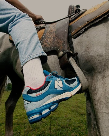 Close-up of a person wearing blue sneakers and light-wash jeans riding a horse in a field.