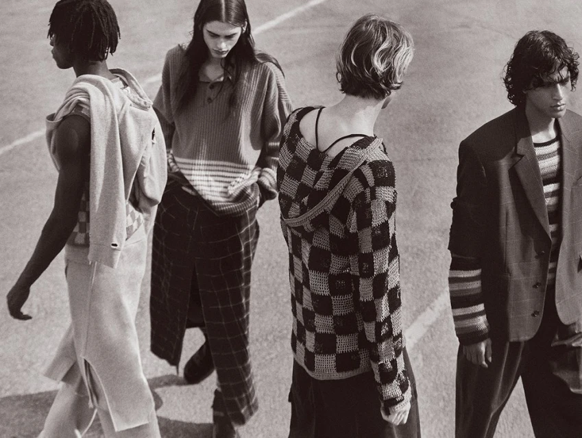 Four fashion models in neutral-toned knitwear walk together in an outdoor setting, showcasing a coordinated and stylish ensemble.