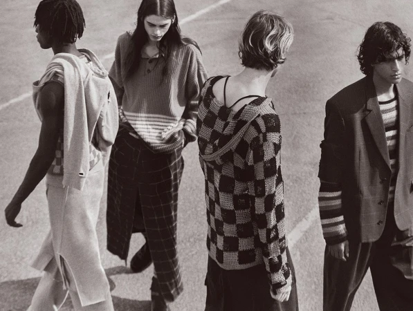 Four fashion models in neutral-toned knitwear walk together in an outdoor setting, showcasing a coordinated and stylish ensemble.