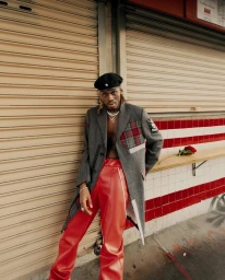 Man wearing a grey wool coat, red leather pants, and a black beret leaning against a closed storefront in Los Angeles.