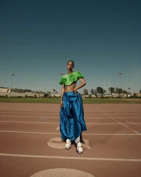 Model standing on a running track wearing a green floral crop top and voluminous blue skirt