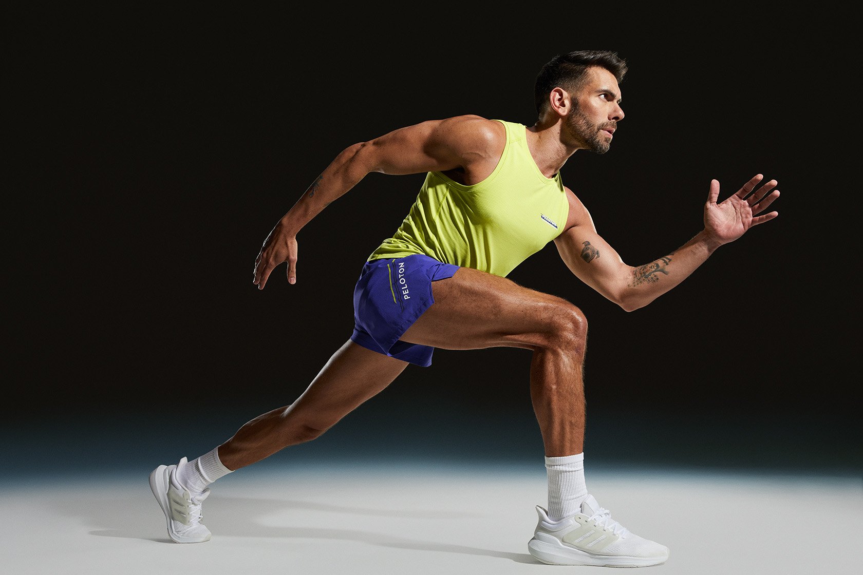 Athletic man in motion wearing Peloton running gear, showcasing strength and fitness in a dynamic studio shot against a dark background.