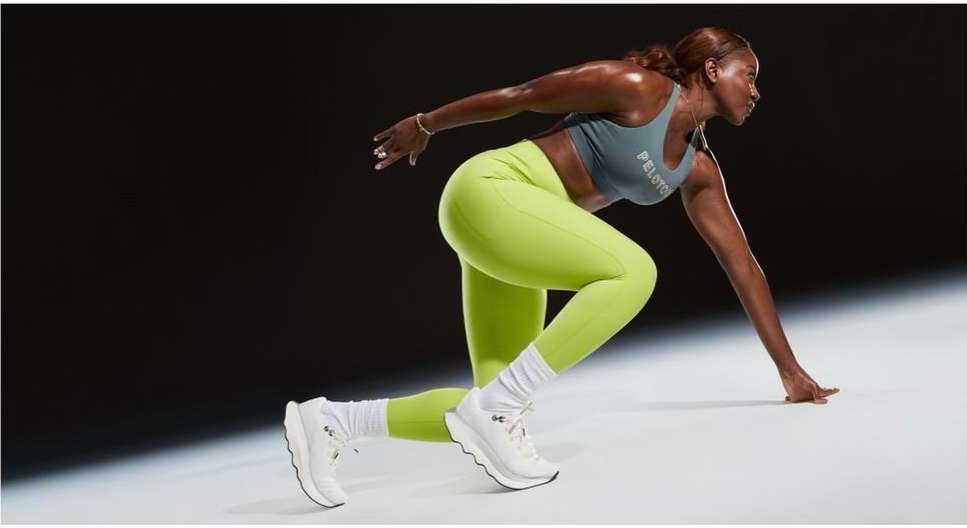 A fit African American woman in activewear is captured in a dynamic studio shot against a dark background, poised in a runner's stance.