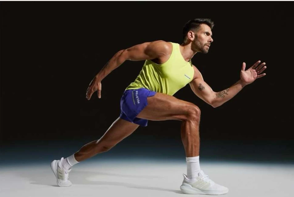 Athletic man running with yellow tank top and blue shorts. Fitness model with white running shoes exercising in a studio.