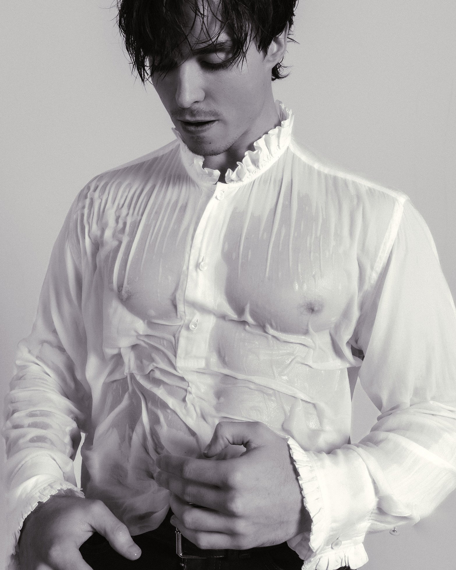 Man wearing a wet white ruffled shirt and dark trousers against a plain white background