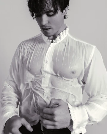 Man wearing a wet white ruffled shirt and dark trousers against a plain white background