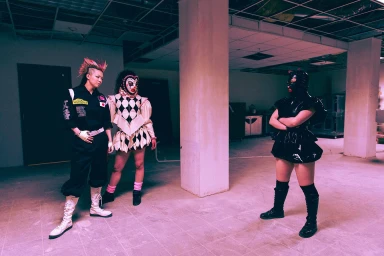 Three costumed individuals standing in an unfinished interior space under pink lighting photographed by Camraface in Los Angeles.