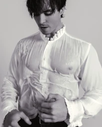 Man wearing a wet white ruffled shirt and dark trousers against a plain white background