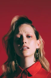 Portrait of a woman wearing a red collared top and large gold earrings against a solid red background by Camraface
