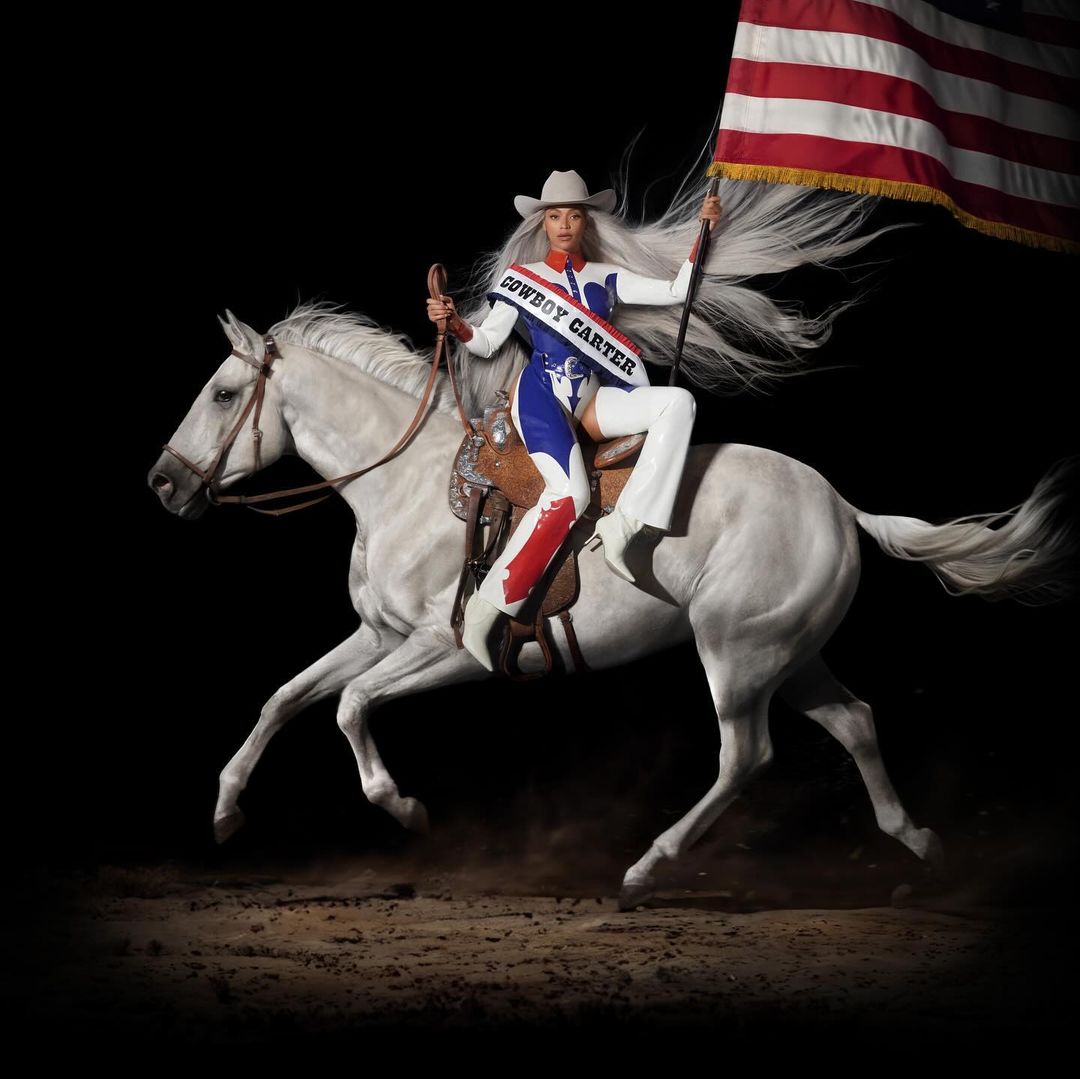 Beyonce on horseback holds an American flag, wearing a cowboy hat and a sash labeled 'Cowboy Carter,' set against a black background.