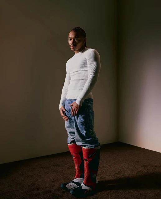 Portrait of a young adult male in a white long-sleeved shirt, baggy jeans, and red motocross boots in a photo studio.