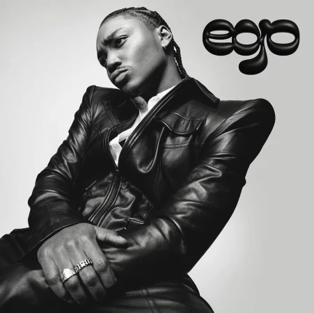 Black and white studio portrait of a young adult with cornrow braids wearing a black leather jacket with the word 'ego' visible.