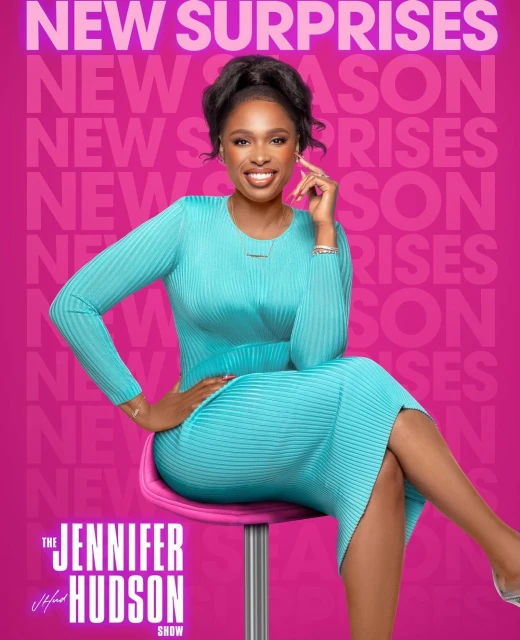 Jennifer Hudson sits on a stool in a blue dress in front of a pink background with the words 'New Surprises' and 'The Jennifer Hudson Show'.