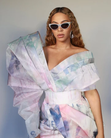 Beyonce wearing cat-eye sunglasses and an off-the-shoulder structured pastel dress against a plain grey background