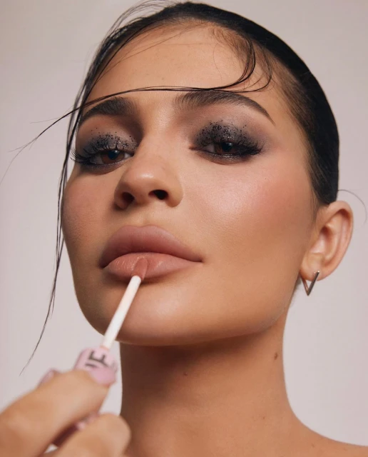 A close-up of a person applying lip gloss with a wand applicator, showcasing makeup details and the product application process.