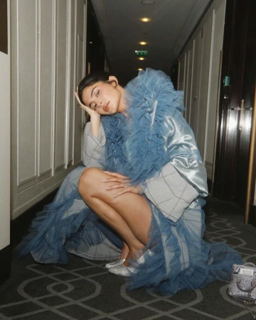 A woman in a blue ruffled coat crouching in a hotel hallway, photographed by Blair Caldwell