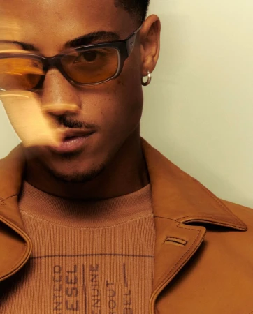 Close-up portrait of a young Black man wearing tinted glasses and a tan leather jacket by Blair Caldwell.