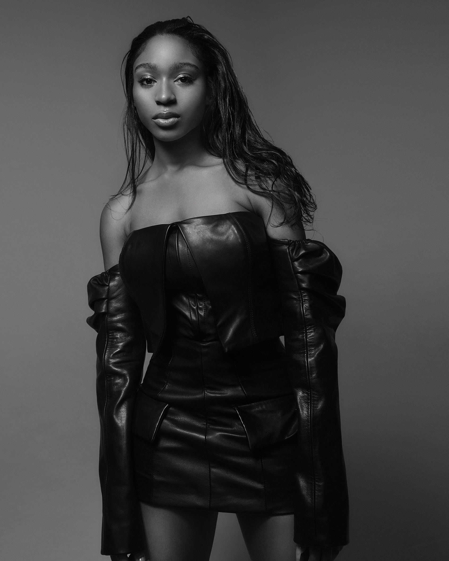Monochrome portrait of a woman in a leather dress with wet hair, posing in a studio setting against a neutral backdrop, fashion shot.