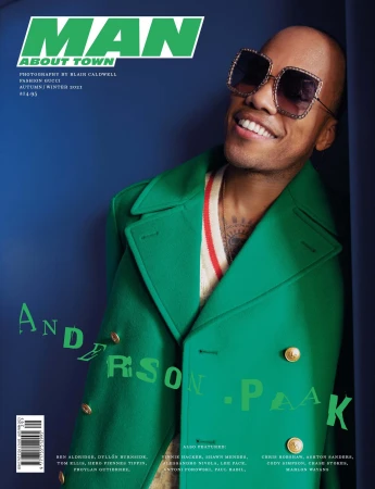 Magazine cover featuring a smiling adult male wearing large sunglasses and a green coat against a dark blue background with text.