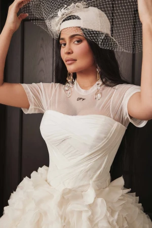 Kylie Jenner wearing a white mesh top, strapless corset, baseball cap with veil, and large crystal earrings by Blair Caldwell