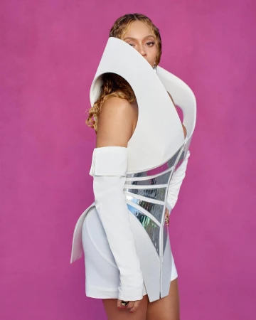Woman with light-brown hair wearing a white futuristic costume with silver accents, posing in front of a pink studio backdrop.