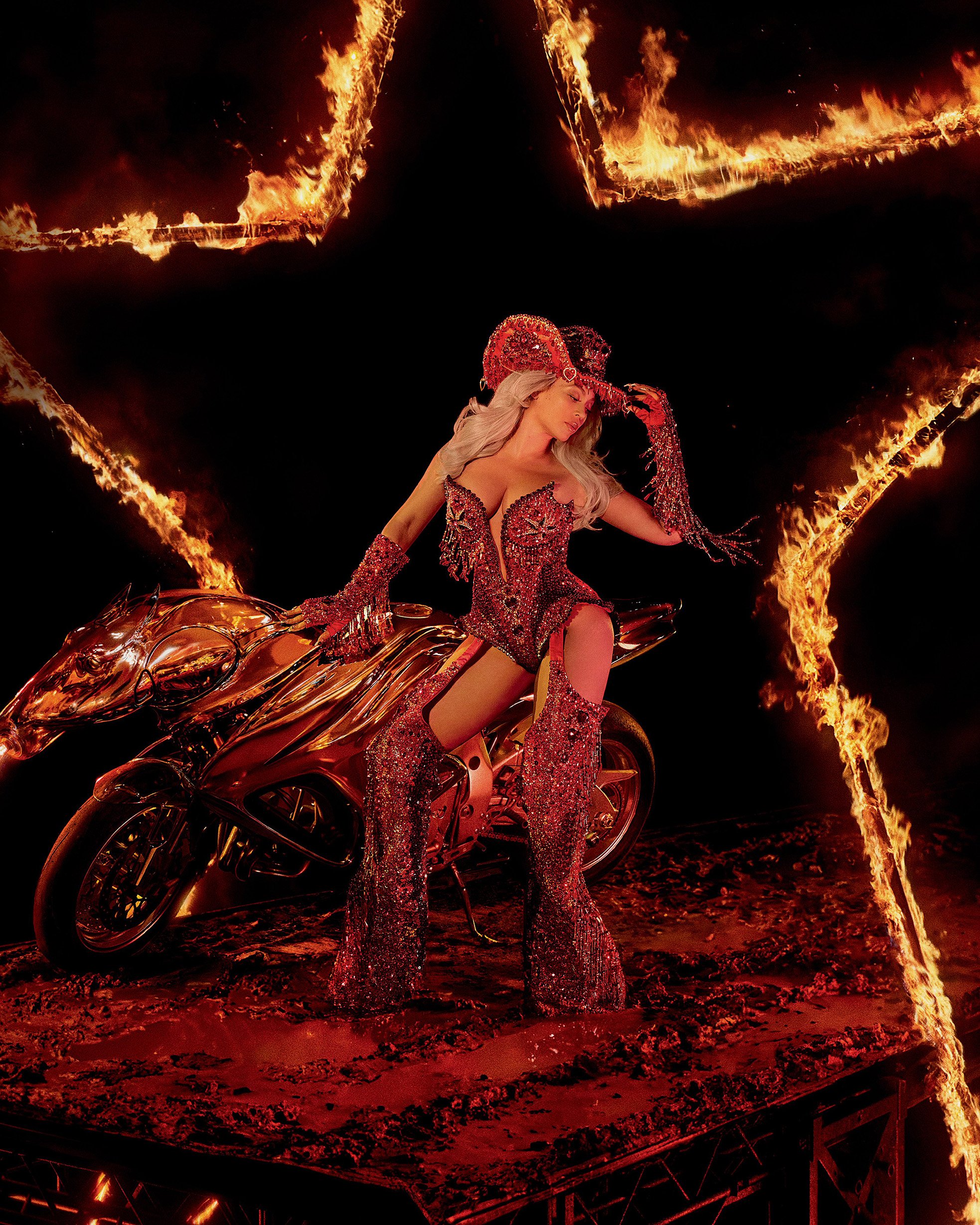 A woman with platinum blonde hair poses on a motorcycle with flames surrounding her, wearing a red rhinestone cowboy hat and outfit.