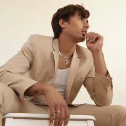A young man wearing a tan blazer and white ribbed tank top posing against a clean white background, photographed by Blair Caldwell.