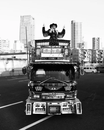 Woman wearing a cowboy hat and fringe jacket standing atop a decorated truck in Los Angeles, photographed in black and white by Blair Caldwell.