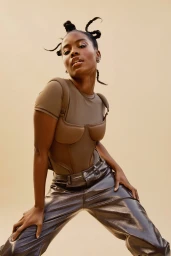Black woman with braided top knots wearing olive green top and glossy brown pants photographed by Blair Caldwell