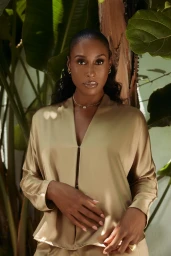 Portrait of Issa Rae wearing a satin gold V-neck top outdoors amidst large green tropical leaves in Los Angeles.
