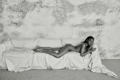 Black woman lying prone on a draped white sofa against a textured concrete wall in Los Angeles by Blair Caldwell.